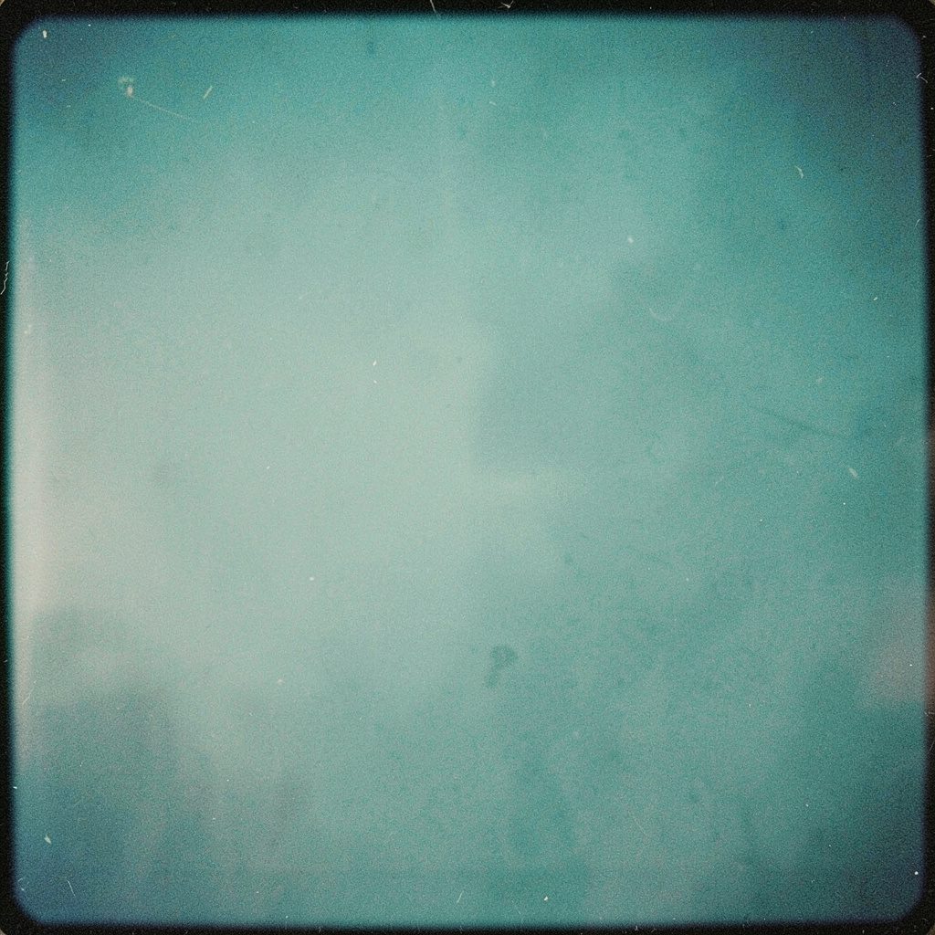 Small square photograph of a folded newspaper on a wooden table, muted sepia tones, documentary mood, film grain
