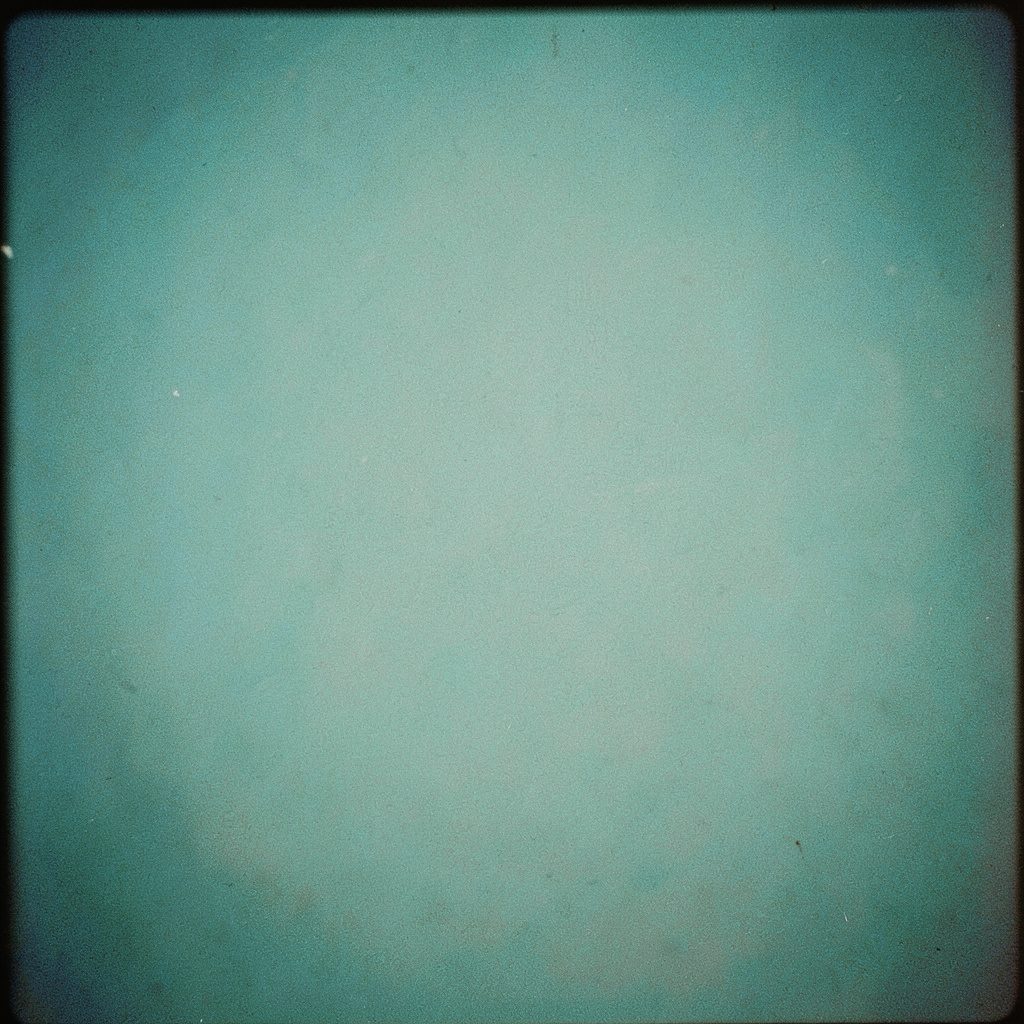 Small square photograph of stacked papers on a grey desk, muted tones, calm academic mood, film grain